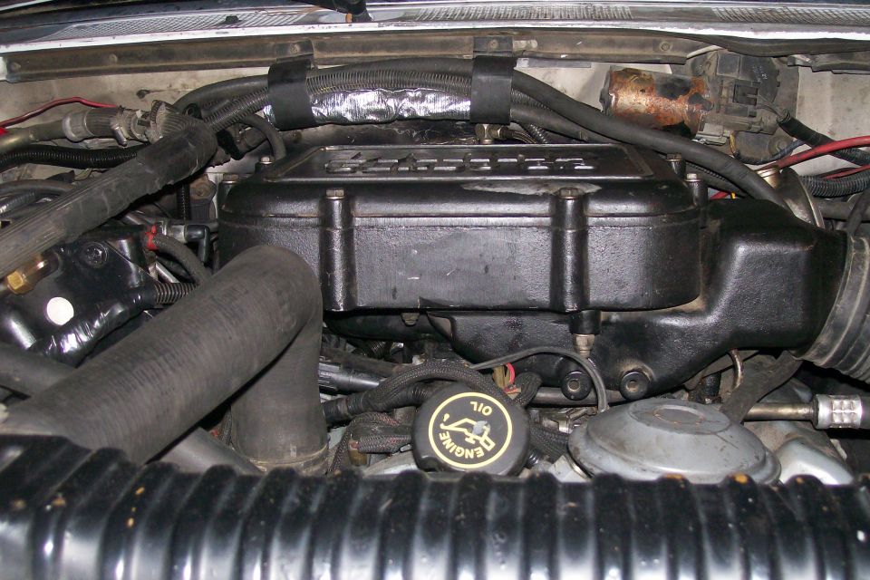 Engine bay with hoses and black engine cover. Oil cap says 'ENGINE OIL'