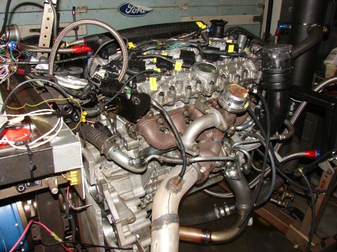 1996 Jeep Grand Cherokee - Engine assembly with turbocharger and wiring, set up for testing. Ford logo in background.