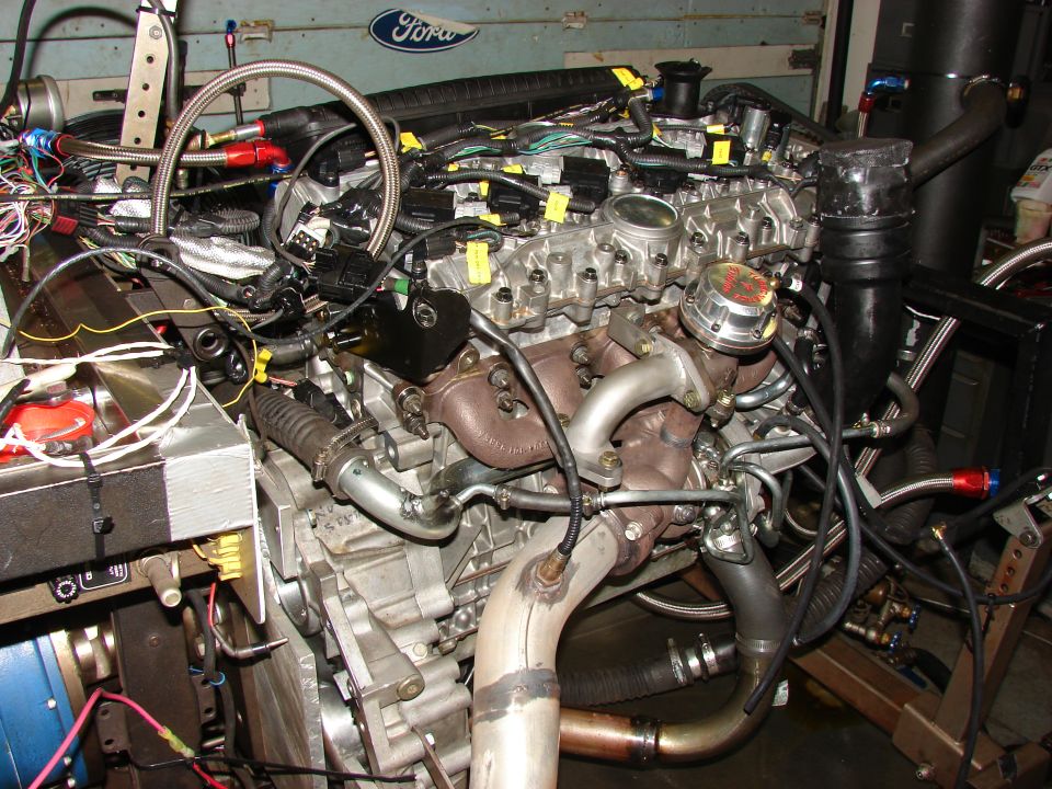 Engine assembly with turbocharger, exhaust manifold, and extensive wiring harness. A Ford logo is visible in the background
