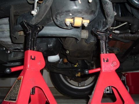 2007 Ford Mustang - The underside of a vehicle is elevated on jack stands, revealing suspension and drivetrain parts.