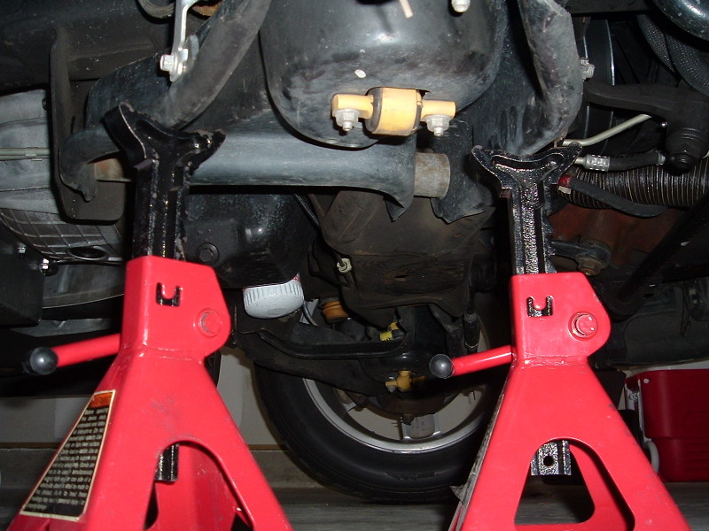 Car underbody with suspension components visible, supported by red jack stands