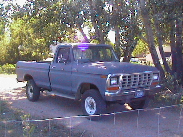 Gray Ford single-cab long-bed 4x4 pickup parked on dirt lot, 3/4 front view