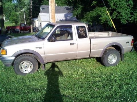 1997 Ford Ranger - Silver/tan Ford Ranger 4x4 extended-cab pickup, side profile, parked on grass with a red truck behind it.