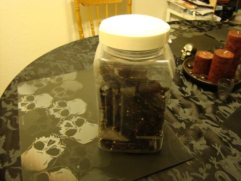 1989 Ford Bronco - A large plastic jar filled with jerky sits on a table covered with a dark, patterned cloth and skull-themed placemats.