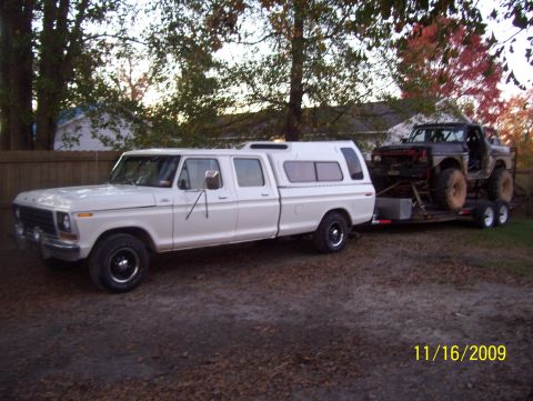 1978 Ford Bronco - White late-1970s Ford crew cab pickup with a matching white camper shell and black steel wheels, shot in profile on a gravel driveway. It i…