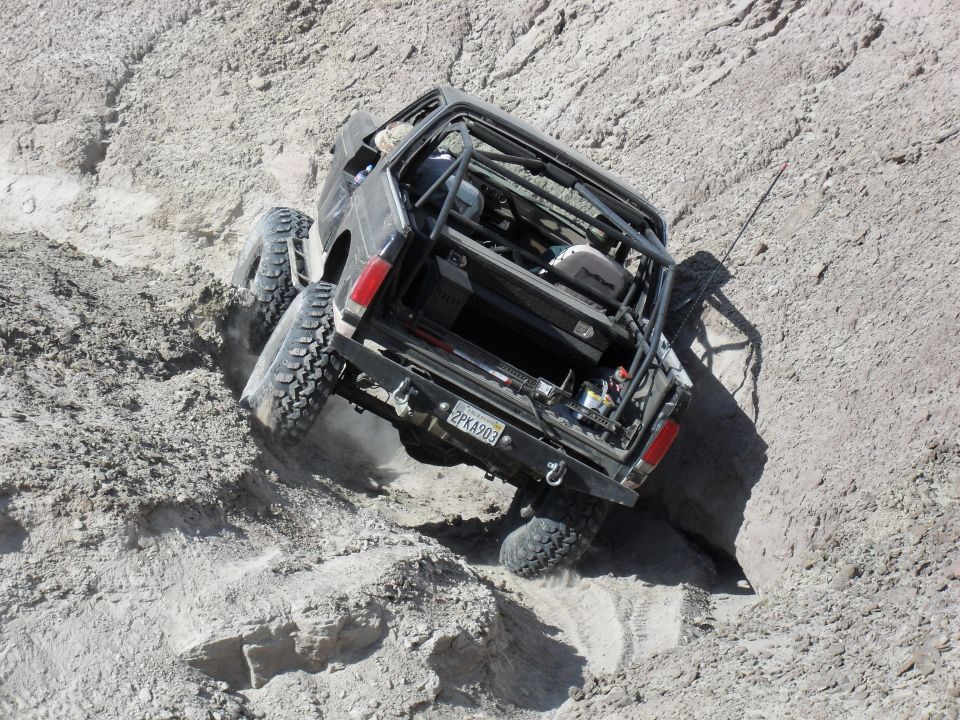 Rear of caged off-road truck climbing a steep eroded dirt hill