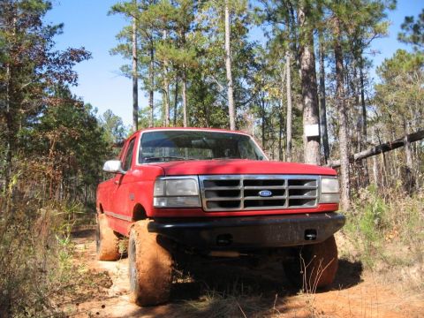 1995 Ford F-150 - Red 1995 Ford F-150 truck with lifted suspension driving off-road.