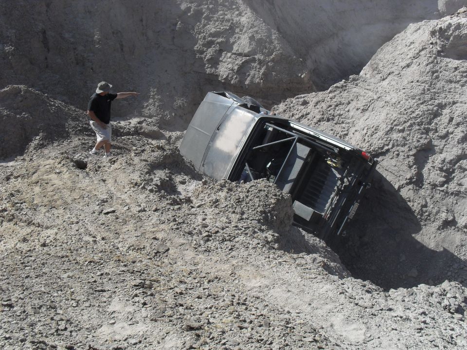 Person watching a vehicle tilted nose-down in an eroded dirt gully