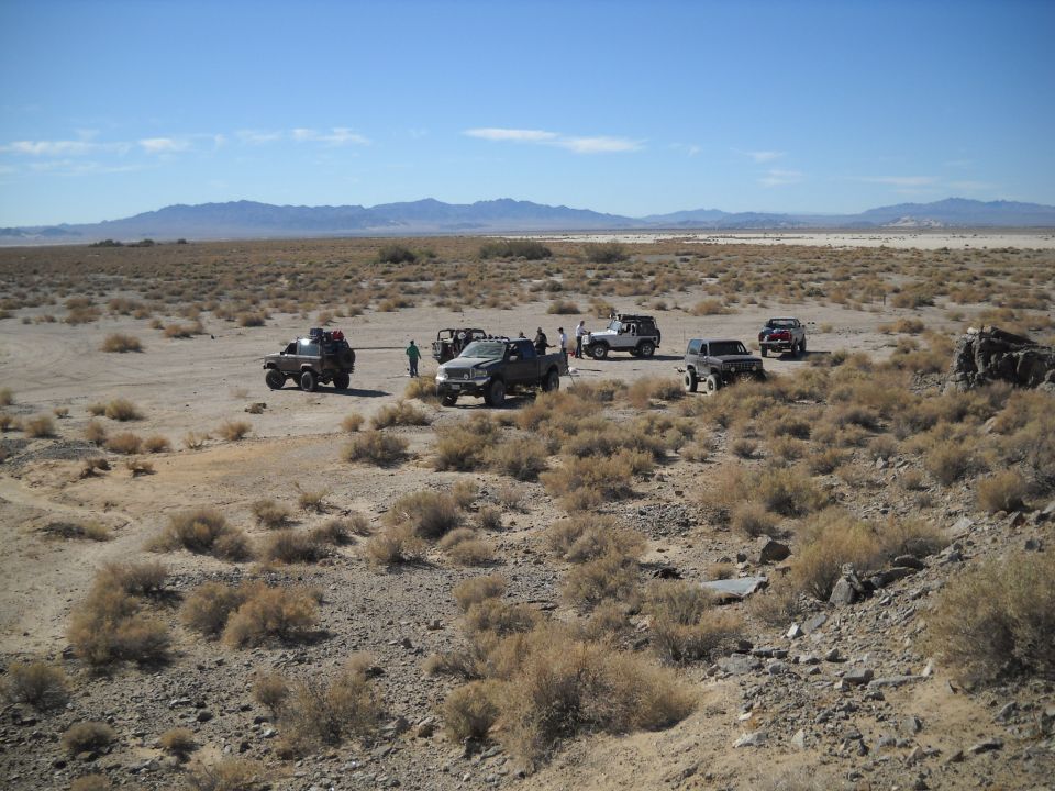 Several off-road vehicles parked in a dry, scrub-covered desert under a clear blue sky