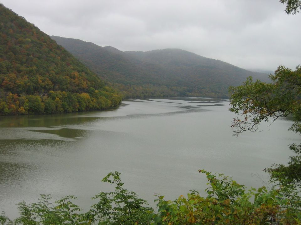 River flows between tree-covered mountains under a cloudy sky