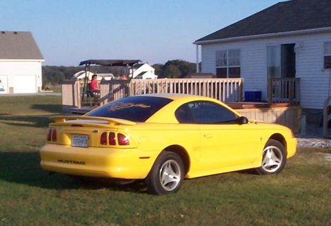 1978 Ford Bronco - A yellow Ford Mustang is parked on a lawn next to a house with a deck.