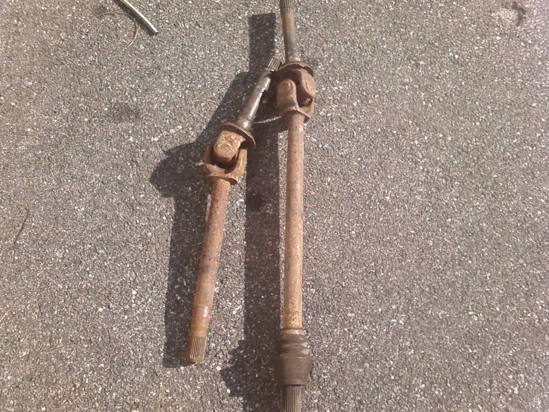 Two rusty driveshafts with universal joints on asphalt