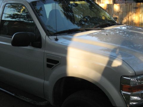 2008 Ford F-250 - A white 2008 Ford F-250 truck is viewed from the front quarter angle, with sunlight casting shadows across its hood.