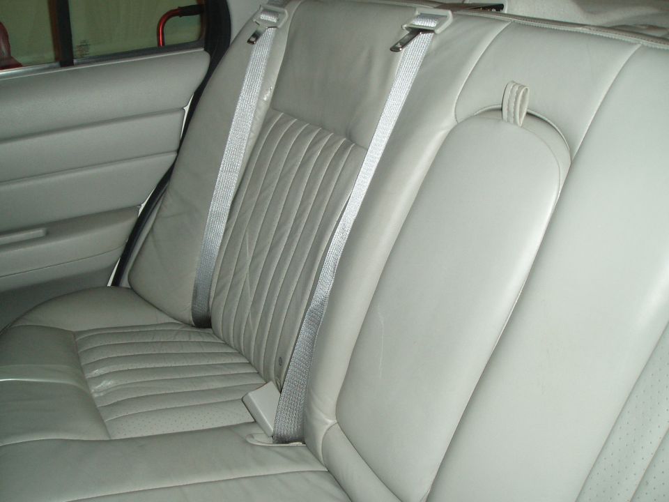 Light gray leather rear bench seat with pleated inserts and gray seat belts in a sedan