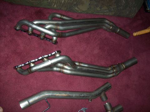 2007 Ford Mustang - Two sets of exhaust headers and a single pipe are displayed on a carpeted surface.