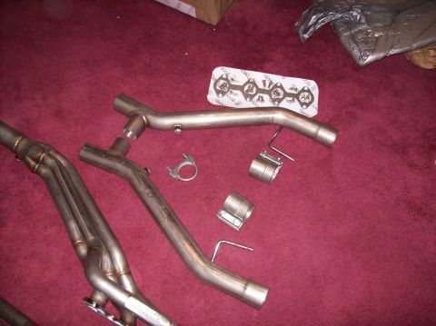 2007 Ford Mustang - A set of long tube headers and a gasket are displayed on a red surface, likely for installation or sale.