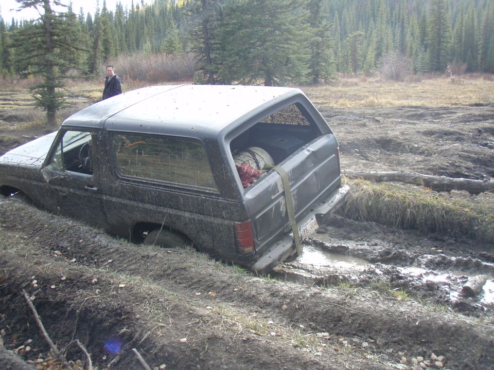 1985 Ford Bronco stuck in mud with trees and a person in the background