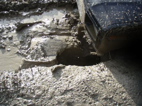 1985 Ford Bronco - A vehicle is stuck in thick mud, with its tire partially submerged.