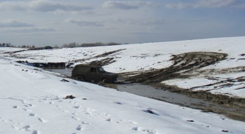 1985 Ford Bronco - A dark-colored SUV navigates a muddy, snow-covered terrain, leaving deep tire tracks.