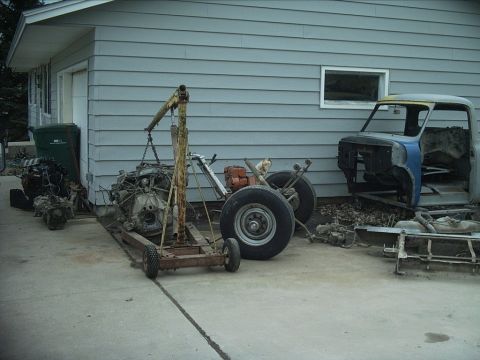 1954 Ford F-100 - Disassembled truck cab and engine on hoist with other parts are stored outside.