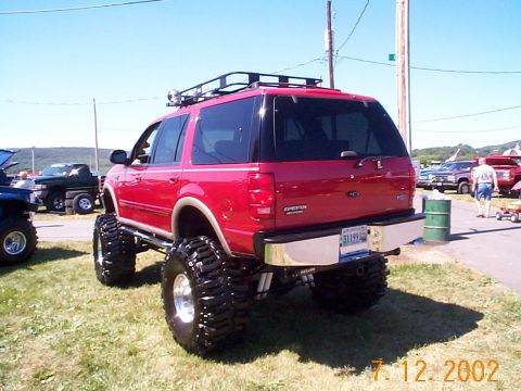 1978 Ford Bronco - Modified red Ford Expedition with oversized tires and roof rack parked on grass at an outdoor event.