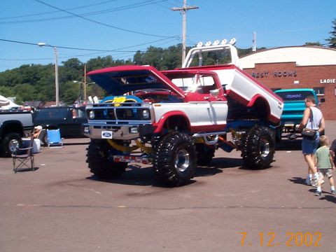 1978 Ford Bronco - This heavily modified pickup truck features a lifted suspension and custom paint, with its hood open at an outdoor event.