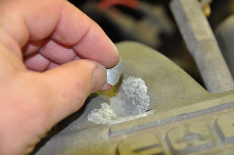 1996 Ford Bronco - A hand removes flaky white corrosion from a vehicle's engine component.