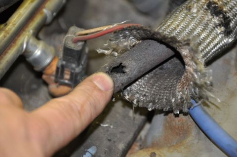 1996 Ford Bronco - A finger points to a hole in a frayed engine wiring harness, revealing damaged insulation.