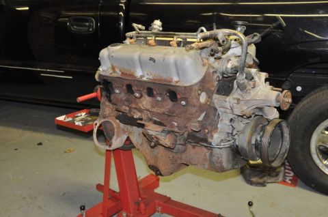 1996 Ford Bronco - A V8 engine, heavily rusted, is mounted on a red engine stand next to a black vehicle.