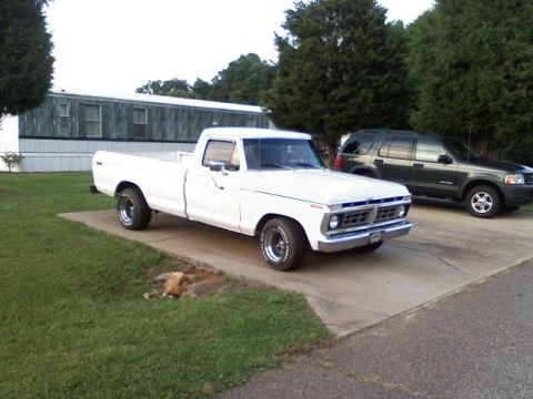 1995 Ford Bronco - White 1975 Ford F-100 pickup truck parked on a concrete driveway next to a dark SUV.