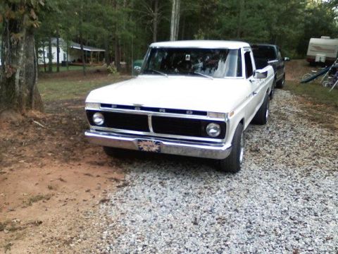 1995 Ford Bronco - A white Ford F-100 pickup truck is parked on a gravel driveway with trees and a house in the background.
