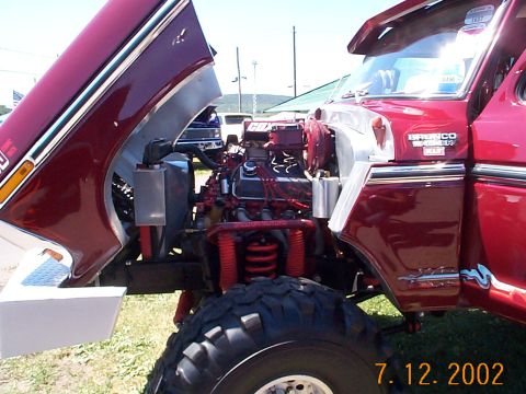 1978 Ford Bronco - The engine bay of a red 1978 Ford Bronco is exposed with the hood raised, revealing its V8 engine and custom suspension.