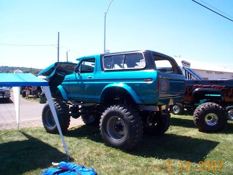 1978 Ford Bronco - A lifted blue 1978 Ford Bronco is parked on grass, with its hood open, under a blue canopy.