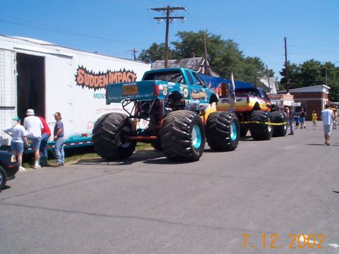 1978 Ford Bronco - Two monster trucks are lined up next to a trailer with "Sudden Impact" graphics.