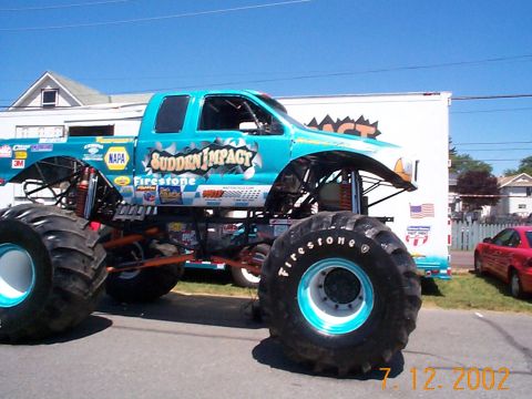 1978 Ford Bronco - A monster truck named 'Sudden Impact' is parked next to a trailer, with a red car visible in the background.