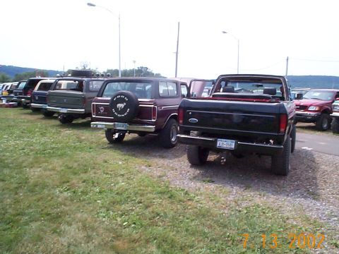 1978 Ford Bronco - A line of Ford trucks and Broncos are parked on a grassy lot, with a street light visible overhead.
