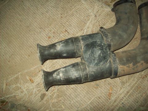 1985 Ford Bronco - Close-up of an exhaust pipe Y-pipe, likely from an older vehicle, resting on a carpeted surface.