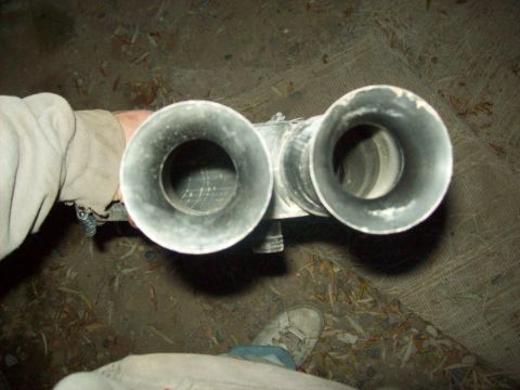 1985 Ford Bronco - A person holds a dual exhaust pipe assembly. The tips are circular and appear to be made of metal.