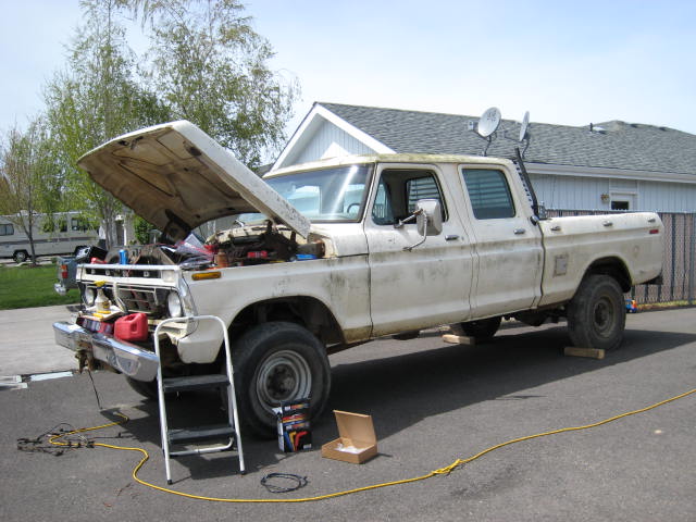 White crew cab pickup with hood raised in driveway, step ladder and tools nearby during repairs