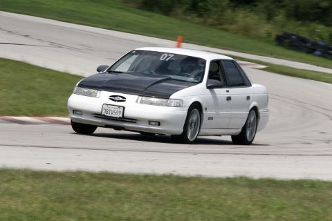 1992 Ford Taurus - A white 1992 Ford Taurus with a black hood navigates a turn on a race track, displaying the number 07.