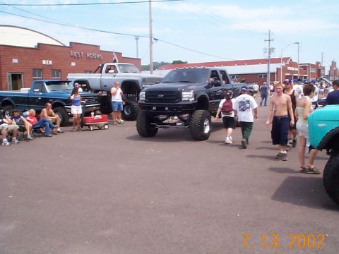 1978 Ford Bronco - Multiple lifted pickup trucks are displayed outdoors with spectators gathered around them.