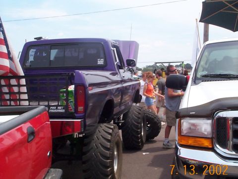 1978 Ford Bronco - A modified purple pickup truck with oversized tires is on display next to a white truck.
