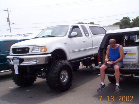1978 Ford Bronco - A lifted 1999 Ford F-150 pickup truck is parked next to another vehicle, with a man sitting in the truck bed.