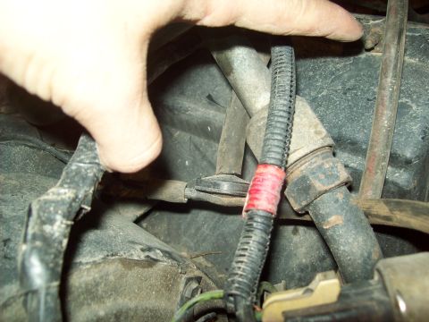 1985 Ford Bronco - A hand manipulates a section of wiring harness in the engine bay, marked with red tape.