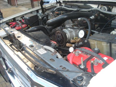 1986 Ford Bronco - Engine bay of a 1986 Ford Bronco, dual batteries and AC system with pressure gauges.