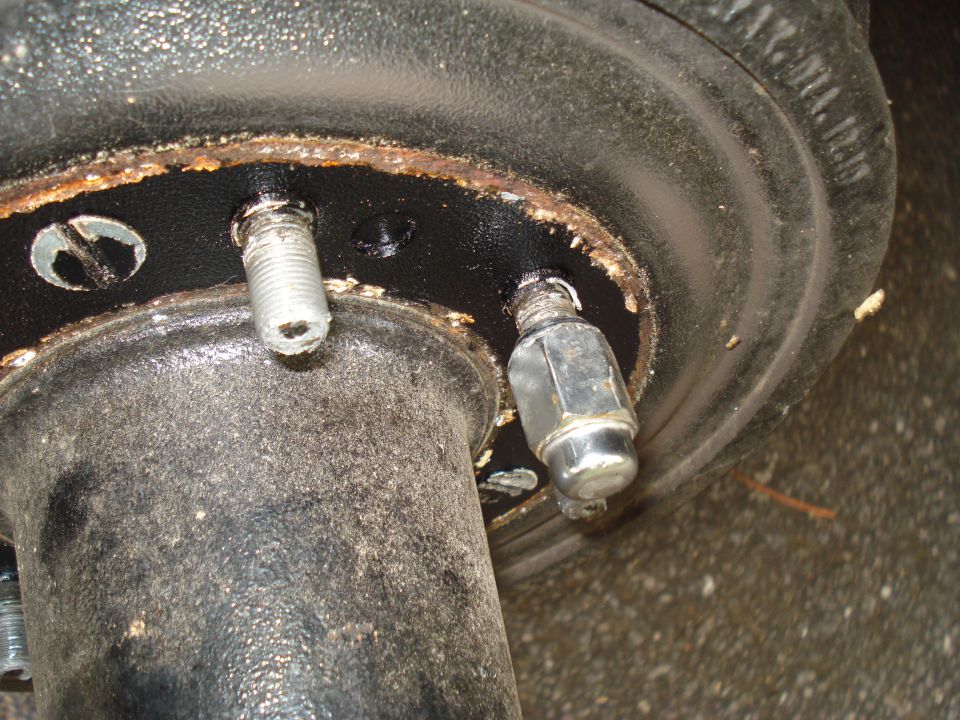 Wheel hub with two exposed lug studs and one lug nut, showing rust and dirt