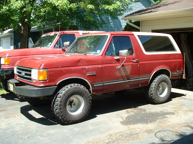 Red and white lifted two-door Ford Bronco SUV on off-road tires in a driveway, 3/4 front view.