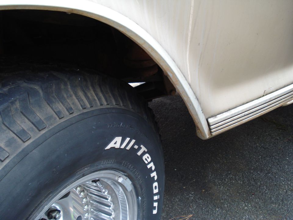 Cream-colored vehicle's rear wheel well and tire with "All-Terrain" text. Chrome rim visible