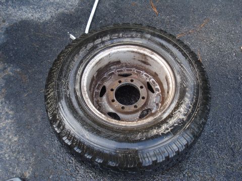 1967 Ford F-250 - A single tire and wheel assembly rests on a wet asphalt surface, showing its tread and rim details.