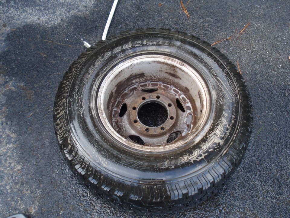 Tire and wheel assembly on asphalt, tire is wet with visible tread pattern and sidewall text